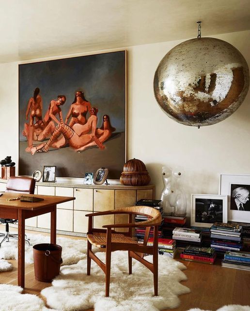 a whimsical home office with an oversized painting, a desk and some chairs, stacks of books, a disco ball and some decor