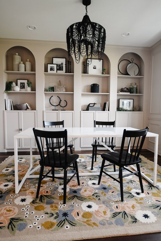 a whimsical home office with tan arched bookcases with black and white decor, a white desk, black chairs and a black chandelier