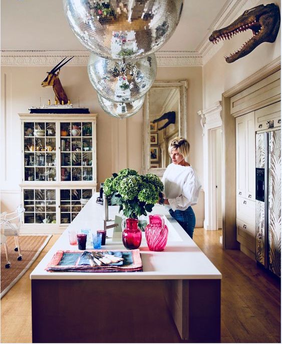 a whimsical kitchen with a large kitchen island and disco balls over it instead of usual lamps and a display piece with taxidermy
