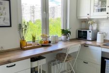 a white Scandinavian kitchen with shaker cabinets, butcherblokc countertops covering the space by the window to create an eating zone