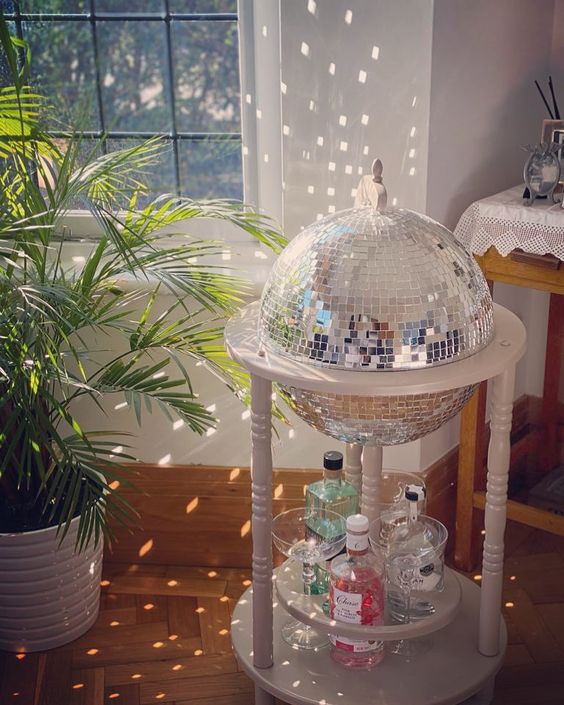a white bar cart with a disco ball and drinks and bottles is a fun and cool idea to add a party feel to the space