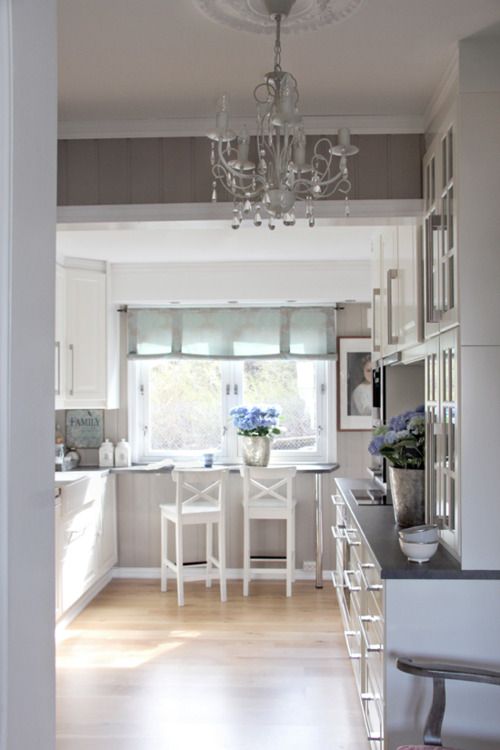 a white farmhouse kitchen with dark countertops, a windowsill table, white stools and a crystal chandelier plus a view