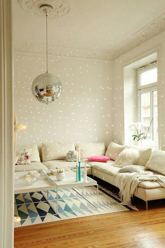 a white living room with a sectional, a couple of tables, a printed rug and a disco ball instead of a chandelier