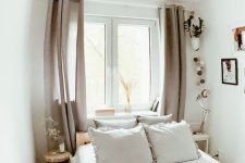 a white narrow bedroom with a bed and neutral bedding, mismatching nightstands, mauve curtains and some decor