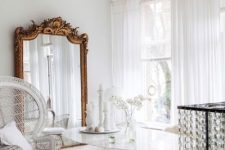 an all-white dining room with a mirror in an ornated frame, a white table and metal and papasan chairs is wow