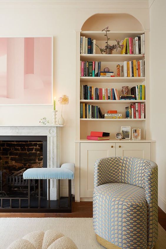 An arched built in bookshelf with a cabinet, a fireplace, a blue stool, a printed cruved chair and an artwork