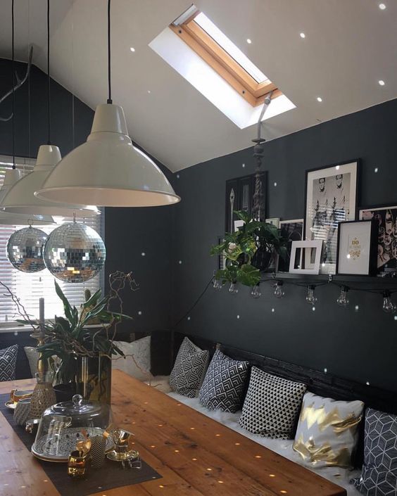 an attic Scandinavian dining room with black walls, a corner sofa with pillows, a table with lamps and disco balls over it