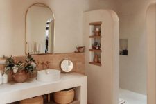 an earthy bathroom with a shower space, a large concrete vanity, a terracotta tile floor, baskets and some decor