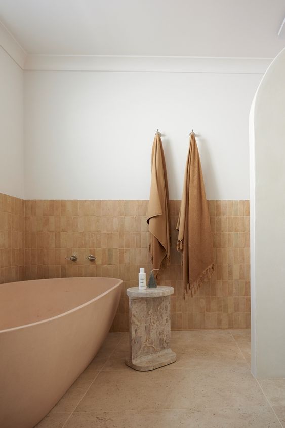 an earthy bathroom with terracotta and stone tile, a blush tub, a shower space and a stone stool is welcoming
