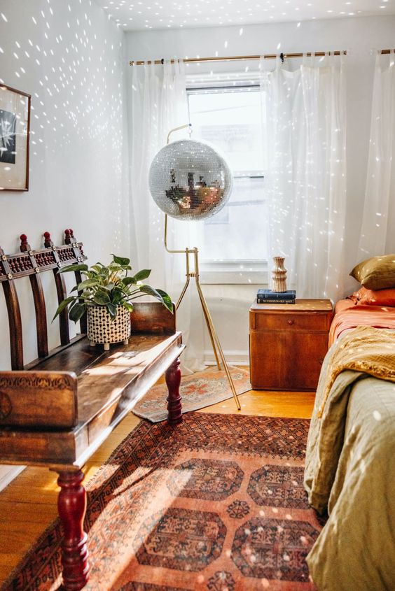 an eclectic bedroom with a bed and bright bedding, a colorful printed rug, a stained bench, a chest and a disco ball suspended