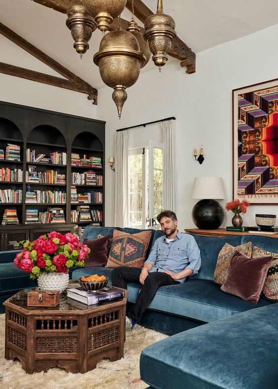 an eclectic living room with black arched bookcases, a navy sectional, a Moroccan table and Moroccan pendant lamps