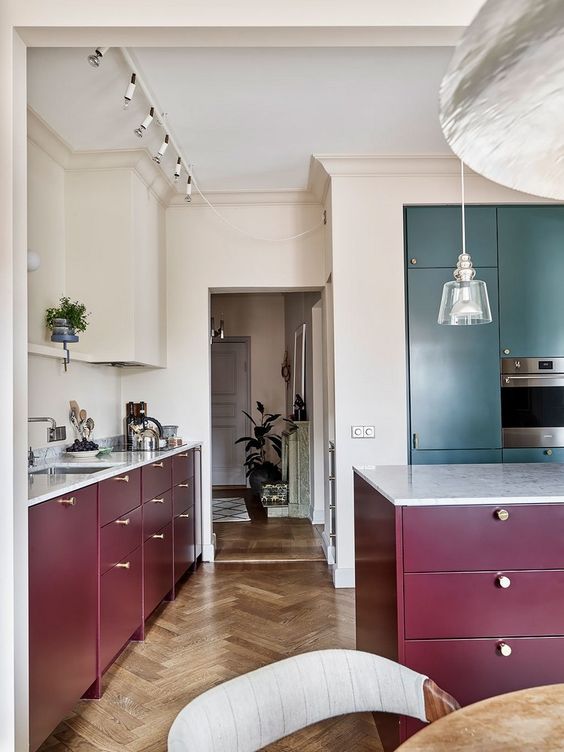 an elegant burgundy kitchen with green cabinetry, white stone countertops and some lights and lamps