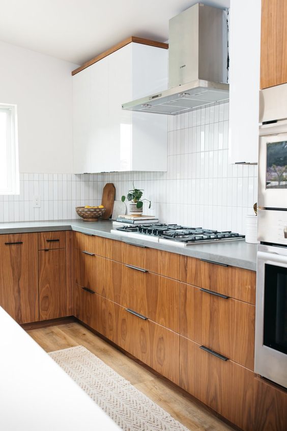 an elegant mid-century modern kitchen with white and stained cabinets, grey countertops and a white stacked tile backsplash