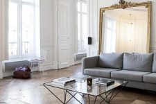 an exquisite Parisian living room with a grey sofa, a leather couch, a glass table and an oversized mirror in a gilded frame