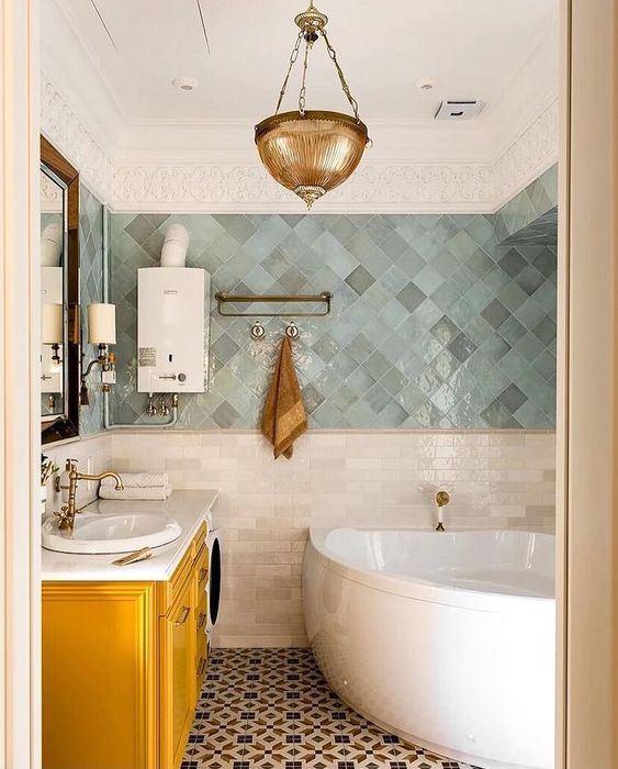 an eye-catchy bathroom done with grey and green Zellige tiles, a corner tub, a yellow vanity, a brass pendant lamp