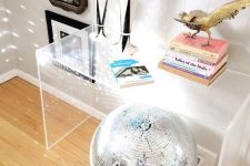 bold home decor with an acrylic console table, a disco ball, some books, a bird figurine, dried flowers in vases