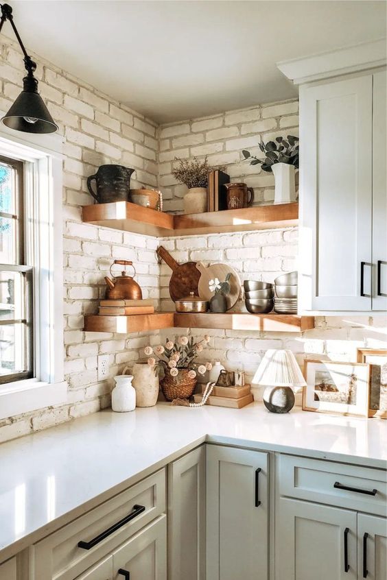 floating stained corner shelves contrast the brick wall and display beautiful tableware and greenery and grasses