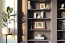 taupe arched bookcases with chic decor, a creamy pouf to contrast and a lovely cat on it