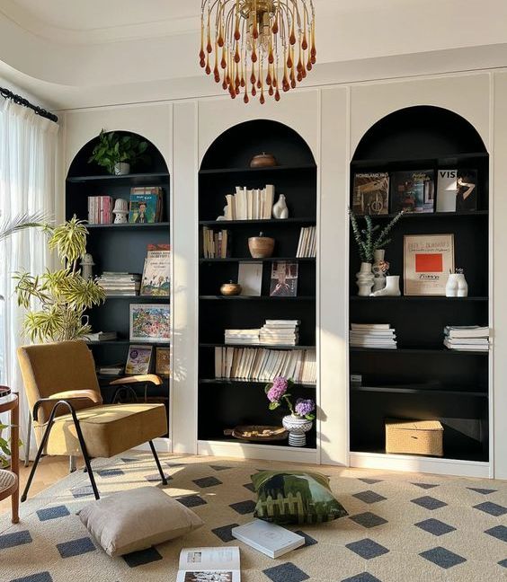white arched bookcases with black backing and shelves, with amazing books and decor, a yellow chair and a rug for a reading nook