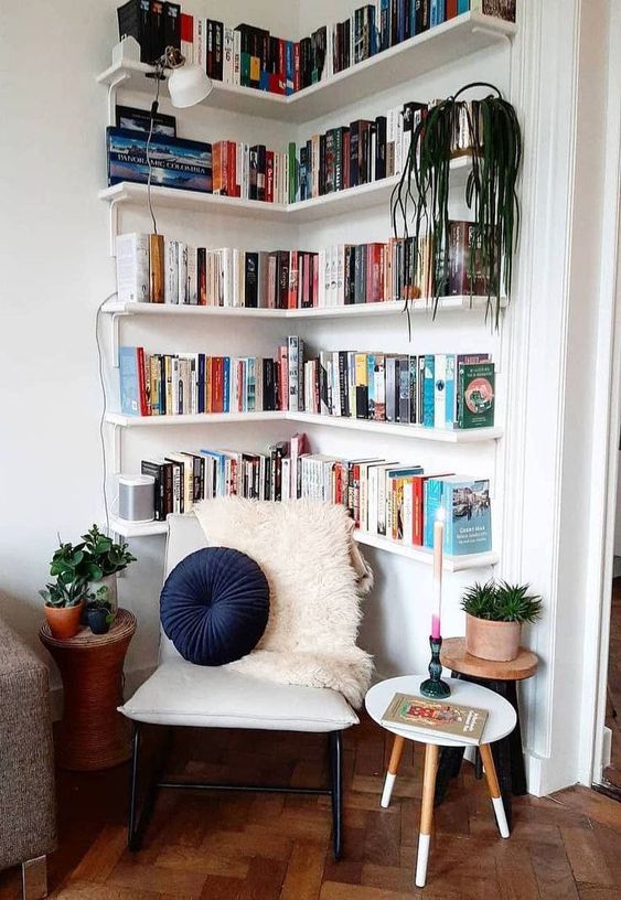 white corner bookshelves, a white chair and some plants make up a very welcoming reading nook in the space