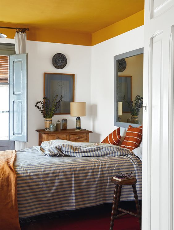 a Mediterranean bedroom with a mustard ceiling, a bed with printed bedding, a stained console table and a large mirror