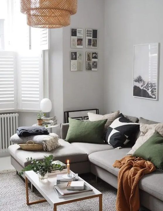 a Nordic living room with light grey walls,a bay window with shutters, a grey sectional with green and other pillows, a coffee table and a woven pendant lamp