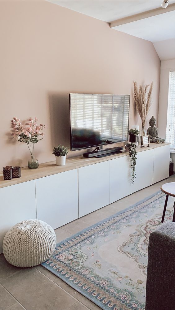 a Scandinavian living room with a blush wall, a large TV unit of IKEA Metod, with a wooden countertop, some decor and potted plants