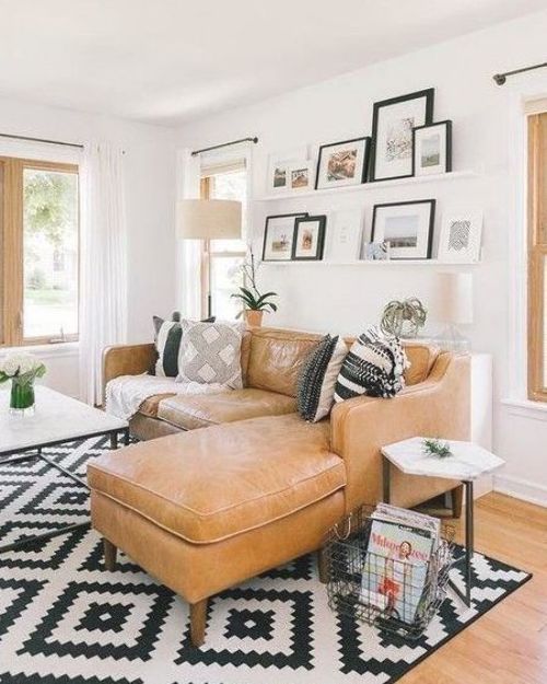 a Scandinavian living room with a tan leather sofa, ledge gallery walls, a printed rug, side tables and lamps