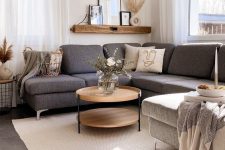a Scandinavian space with a grey sectional sofa, a coffee table, a shelf with decor, a pendant lamp and cozy textiles