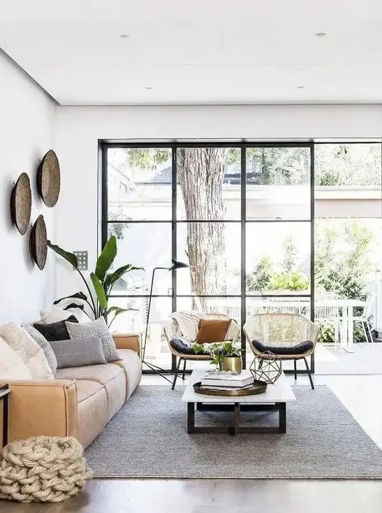 a beautiful living room with a glazed wall, a low tan leather sofa, a low coffee table, rattan chairs and potted plants