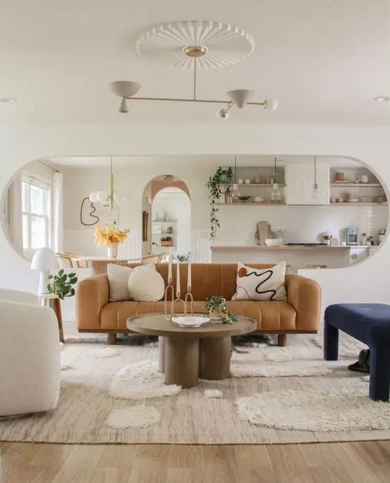 a beautiful living room with a tan leather sofa, a navy upholstered bench, a creamy chair, a large rug and a round coffee table