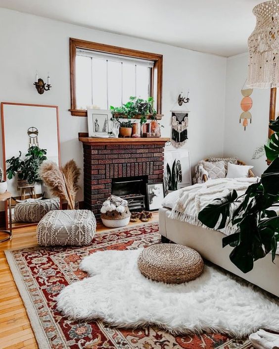 a boho bedroom with a brick fireplace, a bed and layered rugs, floor pillows, a mirror and lots of boho decor