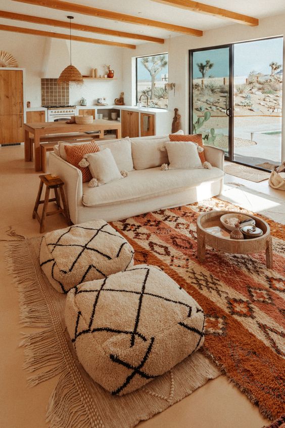 a boho earthy living room with a creamy sofa, layered rugs, a coffee table and some poufs is welcoming