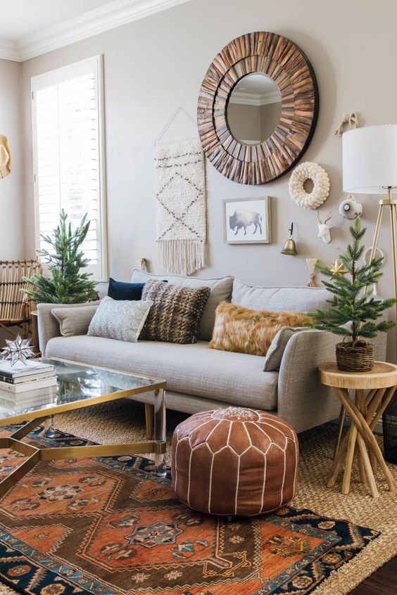 a boho living room with a grey sofa and pillows, a mirror and some boho decor, layered rugs and a coffee table plus some potted plants