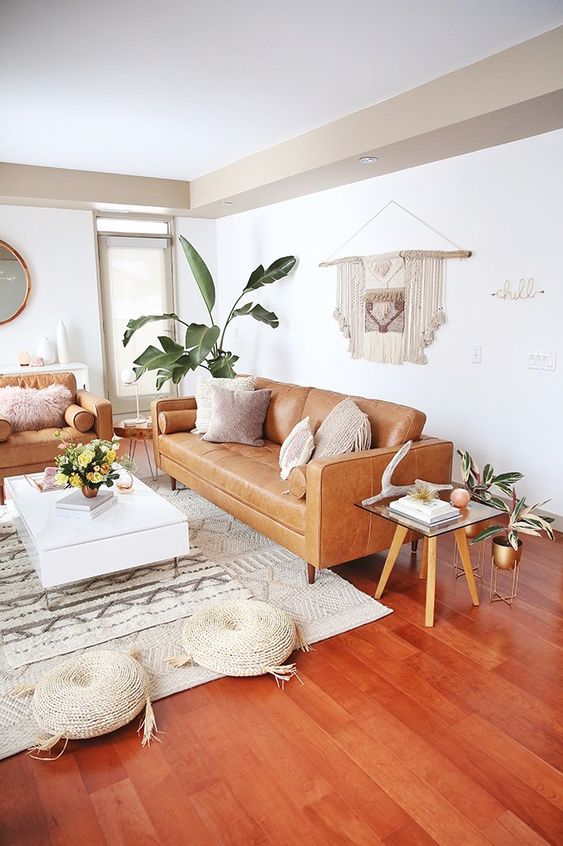 a boho living room with amber leather seating furniture, a coffee table and side tables, potted plants and macrame