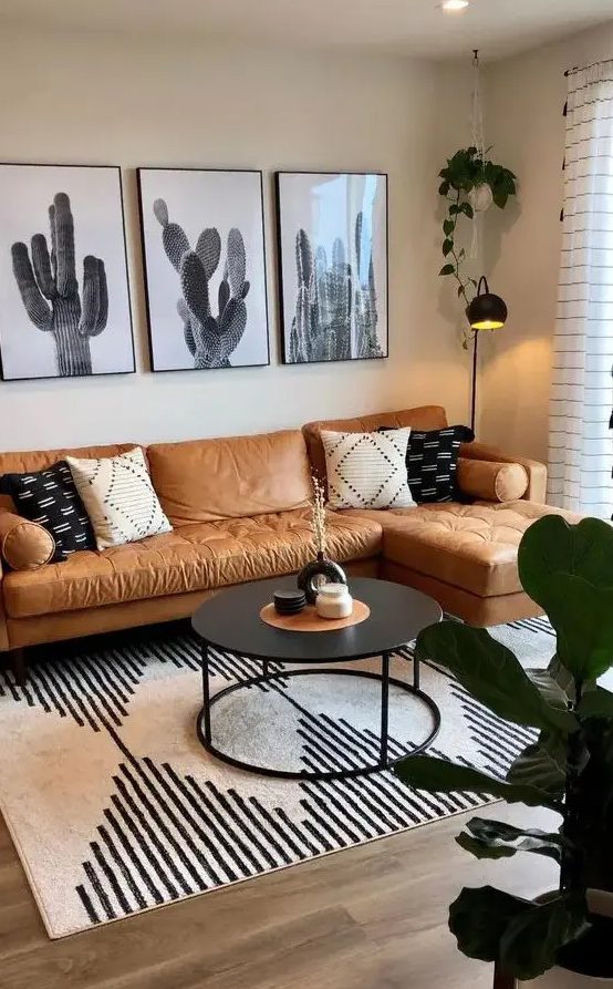 a boho living room with an amber leather sofa, a gallery wall, a black table, a printed rug and some decor