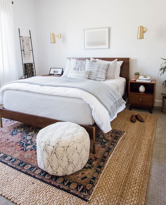 a boho living room with layered rugs, a bed with neutral bedding, nightstands, a ladder, gold sconces and a pouf