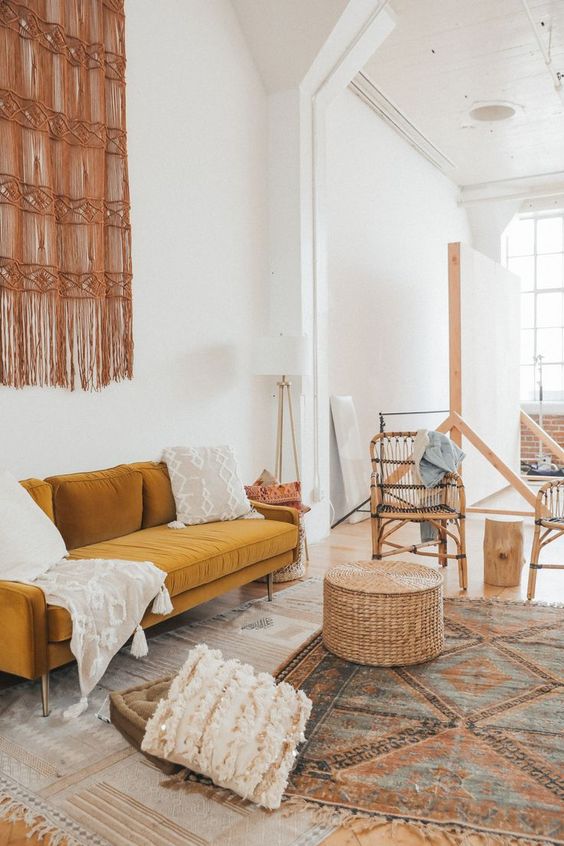 a boho living room with layered rugs, a marigold sofa, baskets and pillows, a macrame and rattan chairs