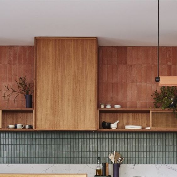a bold kitchen with stained cabinets and a hood, a green skinny tile backsplash, open shelves and terracotta tiles