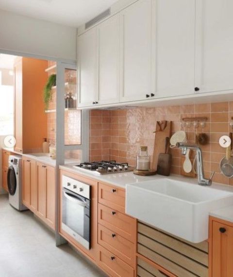 a bold kitchen with white and orange cabinets, white countertops and a glazed terracotta tile backsplash plus black handles