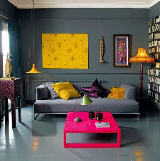 a bold living room with graphite grey walls, a floor and a sofa, bold yellow touches and a hot pink coffee table
