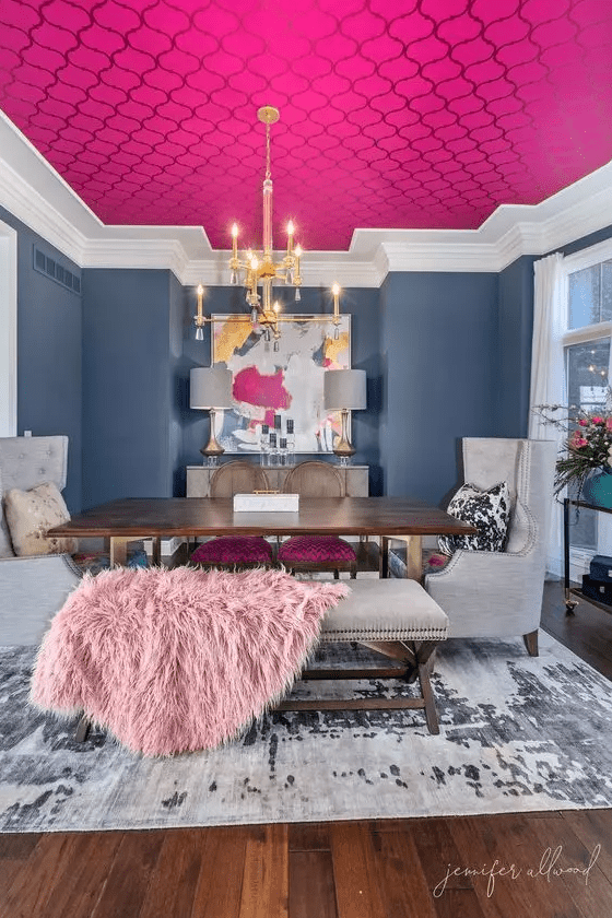 a bright formal dining room with navy wlals, a hot pink printed wallpaper ceiling, a stained table and neutral chairs plus a bold artwork