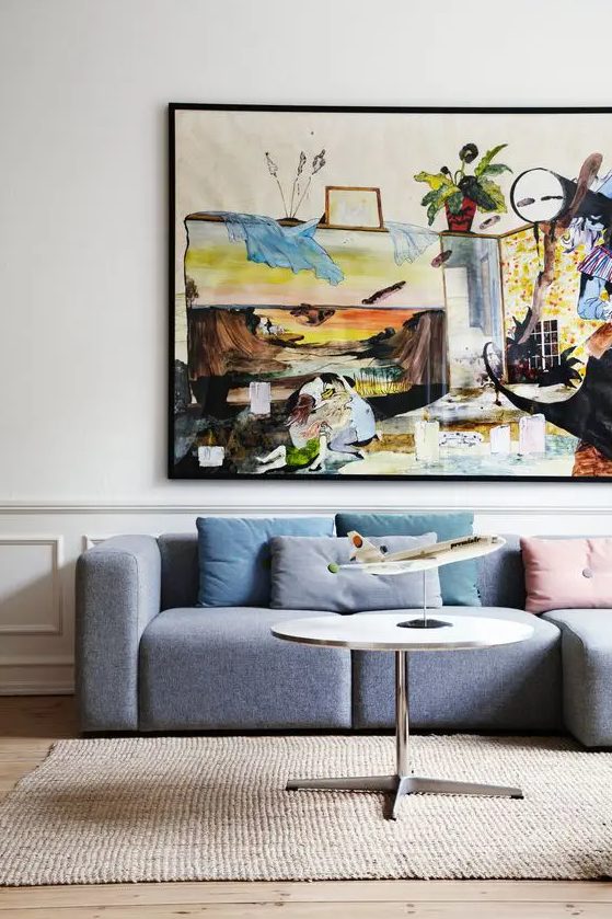 a bright living room with a grey low sofa, a colorful artwork, pastel pillows, a round table is a very cool and bold space