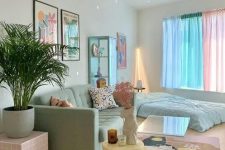 a candy-colored living room with a mint sofa and a bed, pastel curtains, a pink side table, a yellow side table, a pastel printed rug and bold artwork