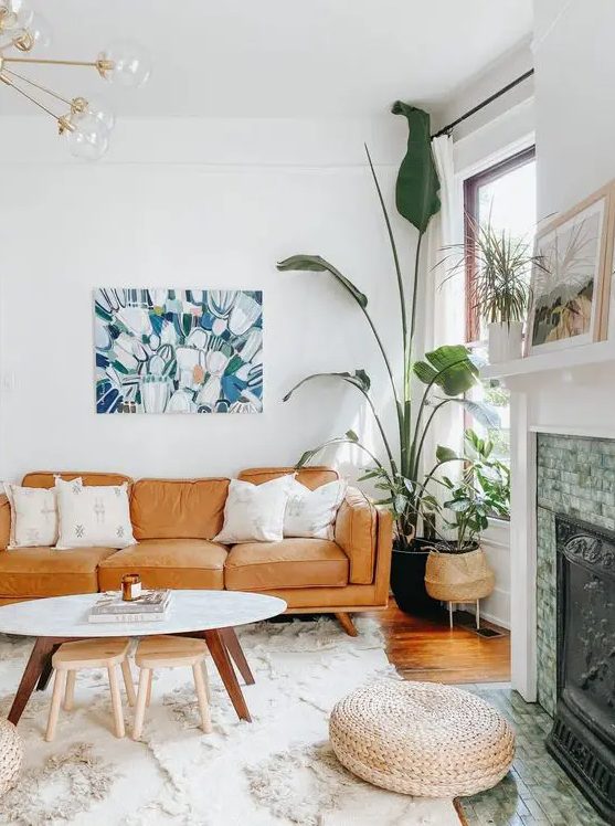 a catchy boho living room with a tan sofa, a coffee table with stools, potted greenery and a non-working fireplace