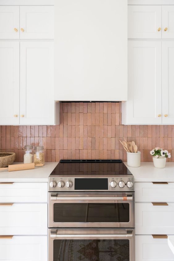 a chic creamy kitchen with shaker style cabinets, white countertops, gold handles and a glazed terracotta tile backsplash