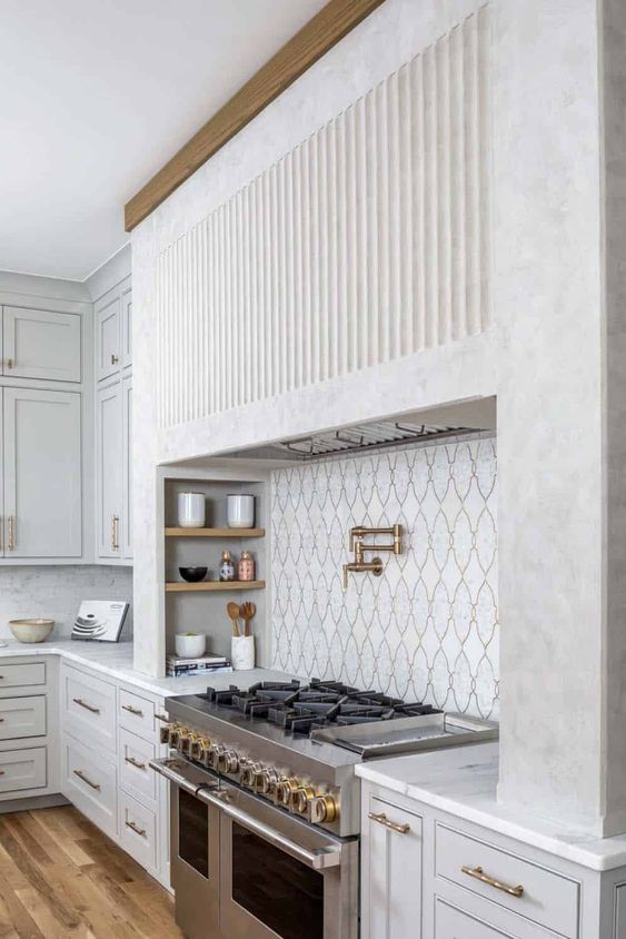 a chic dove grey and white kitchen with shaker cabinets, a large built-in fluted hood and built-in appliances