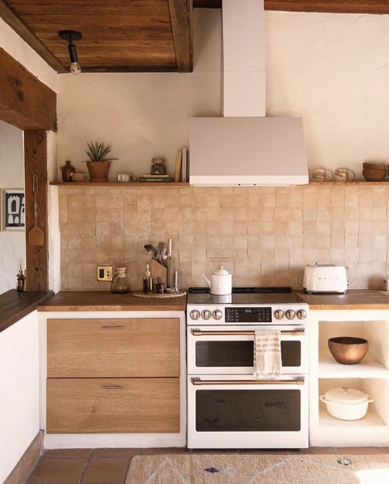 a chic earthy kitchen with white and stained cabinets, a terracotta tile backsplash and butcherblock countertops, open shelves and metal appliances