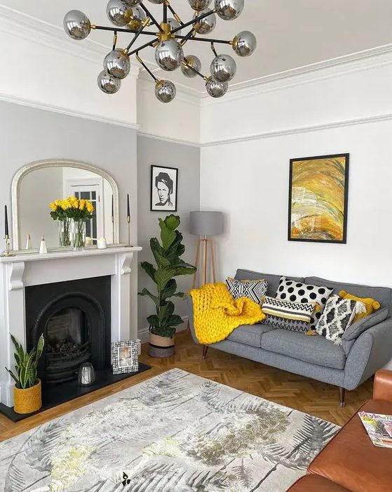a chic living room with a grey accent wall, a fireplace, a grey sofa with printed pillows, a bold artwork and a rug