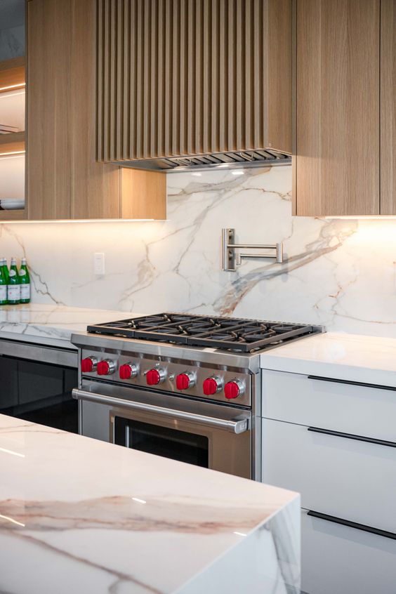 a chic modern kitchen with white countertops, a white stone backsplash and countertops, open shelves and a fluted hood